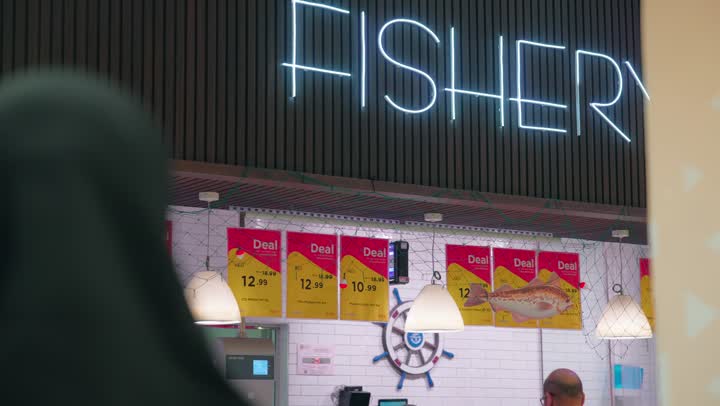 Buying fresh meat from the butcher section inside the supermarket, a rear view of a veiled Emirati Gulf Arab woman standing in front of the meat display fridge and selecting household needs, the concept of family shopping and purchasing fresh food items, preparing orders and customer service inside the store.