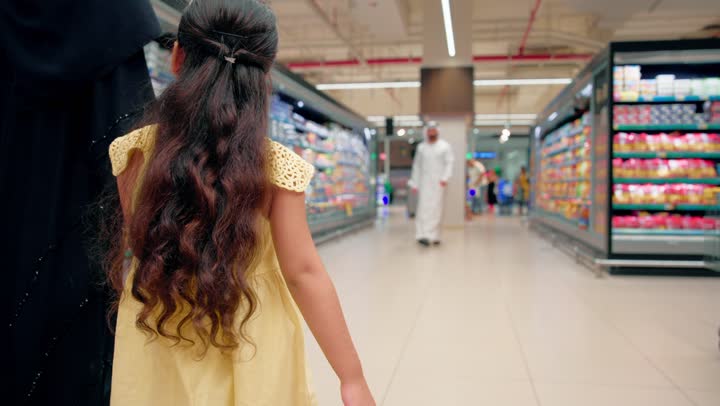 أجواء عائلية سعيدة وقضاء وقت ممتع أثناء شراء الاحتياجات اليومية، التسوق العائلي داخل السوبر ماركت، أب عربي خليجي اماراتي يرتدي الزي التقليدي يقوم باحتضان ابنته داخل الممرات، ايماءات تدل على السعادة والفرحة، مفهوم الترابط الأسري وتقوية العلاقة بين الآباء والأبناء