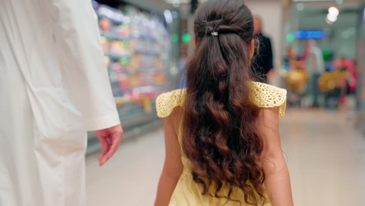 بنت عربية خليجيه اماراتية ترتدي فستان تمشي برفقة والدها وتقوم بعناق والدتها، ايماءات السعادة و السرور ، مفهوم الترابط الأسري والأمومة، التسوق العائلي وقضاء وقت ممتع أثناء شراء الاحتياجات اليومية من السوبر ماركت