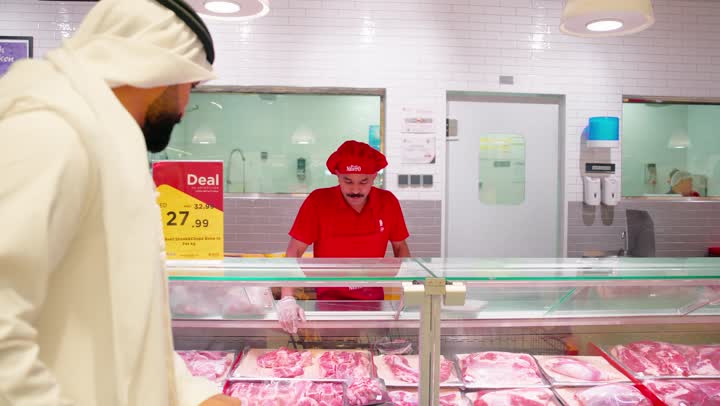 شراء اللحوم الطازجة داخل السوبر ماركت، رجل عربي خليجي اماراتي يرتدي الثوب التقليدي يقف أمام ثلاجة عرض قسم اللحوم والدواجن ، التسوق اليومي واختيار المنتجات الطازجة بعناية، مفهوم شراء المواد الغذائية من أقسام السوبر ماركت، خدمة العملاء داخل المتجر