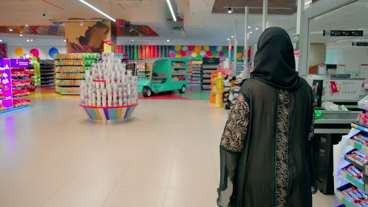 مفهوم التسوق المنزلي والشراء من المتاجر، اختيار المنتجات ومتابعة العروض، تصوير من الخلف لامرأة عربية خليجيه اماراتية محجبة تتجول داخل السوبر ماركت، قضاء وقت ممتع بالتسوق
