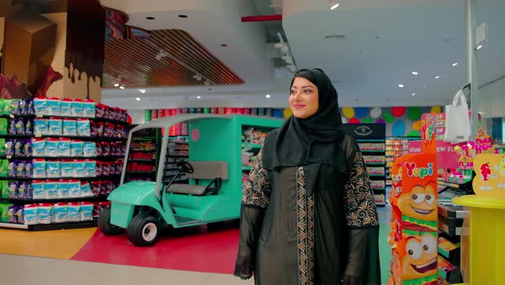 Choosing products and following offers, a veiled Emirati Gulf Arab woman is wandering inside the supermarket, the concept of home shopping and buying from stores, having a good time shopping.