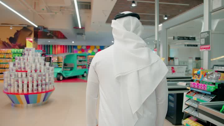 التسوق اليومي وشراء الاحتياجات الأساسية، قضاء وقت ممتع بالتسوق، الاستعداد لاختيار المنتجات ومقارنة الأسعار داخل السوبر ماركت، تصوير من الخلف لرجل عربي خليجي اماراتي يرتدي الثوب الأبيض والغترة يسير داخل السوبر ماركت