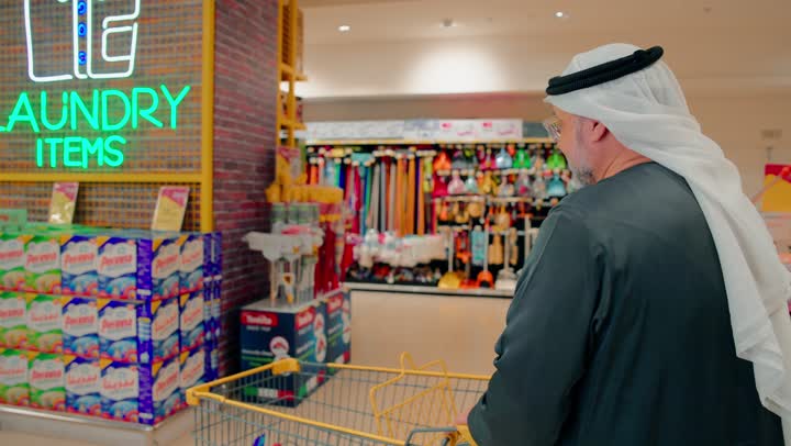 Comparing products and offers inside the store, an elderly Emirati Gulf Arab man is choosing laundry powder and detergents from the supermarket shelves, purchasing household cleaning supplies, daily shopping and caring for home cleanliness, the concept of consumption and household needs.