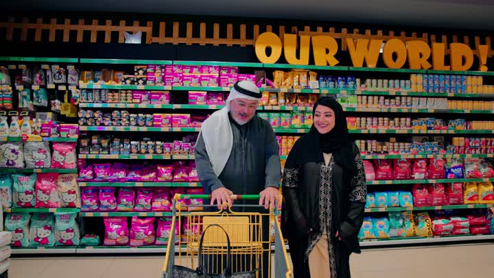 شراء الاحتياجات المنزلية والمواد الاستهلاكية، رجل عربي خليجي اماراتي مسن يرتدي الكندورة و الغترة يقوم بالتسوق داخل سوبر ماركت برفقة ابنته، استخدام عربة التسوق داخل المتجر، مفهوم التسوق العائلي والتخطيط للاحتياجات