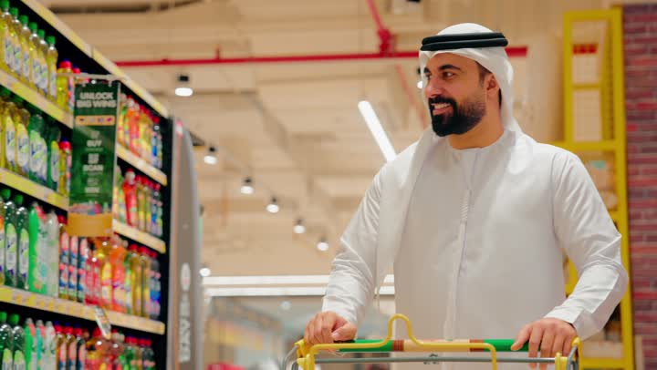شراء متطلبات المنزل، تصوير مقرب لرجل عربي خليجي اماراتي يرتدي الزي التقليدي يجر عربة التسوق داخل السوبرماركت، الاستفادة من العروض والخصومات على المنتجات