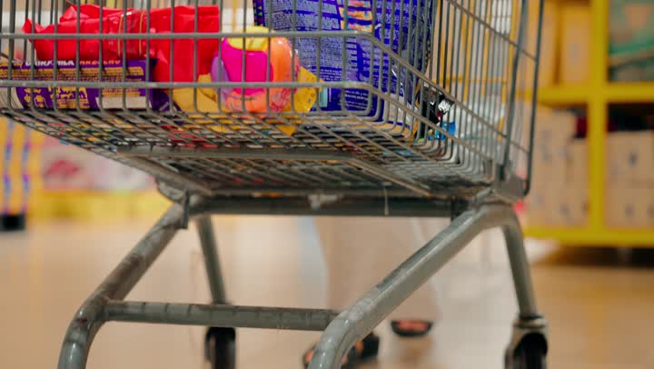 شراء المستلزمات المنزلية، تصوير مقرب لرجل عربي خليجي اماراتي يرتدي الزي التقليدي يجر عربة التسوق داخل السوبرماركت، الاستفادة من العروض والخصومات على المنتجات