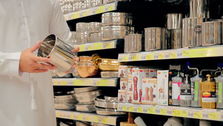 اختيار أواني مطبخ مصنوعة من الستانلس ستيل، تصوير مقرب ليد رجل عربي خليجي اماراتي يرتدي الزي التقليدي يفحص وعاء معدني داخل متجر أدوات منزلية، التأكد من جودة أدوات الطهي قبل الشراء، التسوق داخل مركز تجاري، تجهيز المطبخ المنزلي بأدوات عملية