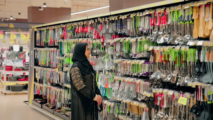 تجهيز المطبخ المنزلي، اختيار أدوات المطبخ المختلفة، سيدة عربية خليجيه اماراتية ترتدي العباءة و الحجاب تتسوق داخل متجر أدوات منزلية، تفقد مستلزمات الطهي الحديثة، التسوق داخل المركز التجاري