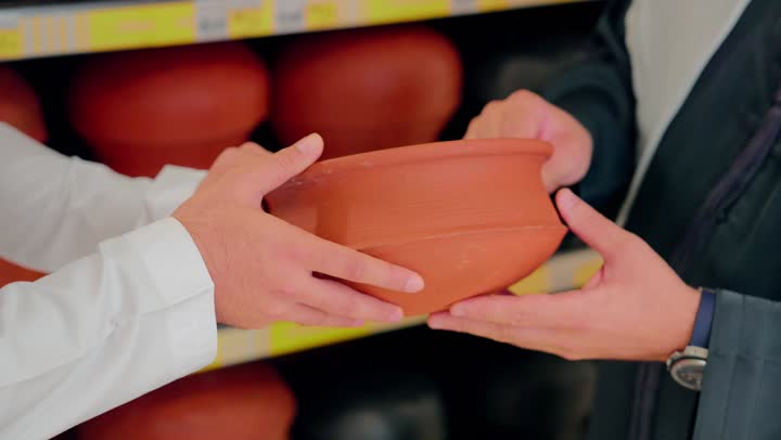 Joint shopping inside the mall, choosing cooking utensils made of natural clay, collaborating in selecting kitchen supplies, focusing on healthy cooking and traditional tools, a close-up shot of an Emirati Arab couple inspecting clay pots inside a home goods store.