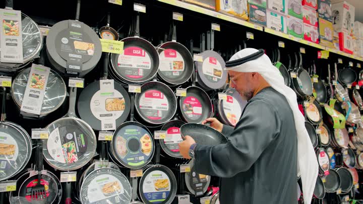 التسوق الفردي داخل المركز التجاري، رجل عربي خليجي اماراتي مسن يرتدي الكندورة و الغترة يتفقد المقالي وأواني الطبخ داخل متجر أدوات منزلية ، اختيار أدوات مطبخ مناسبة للاستخدام اليومي، الاهتمام بتجهيز المطبخ بأواني عملية ومتينة
