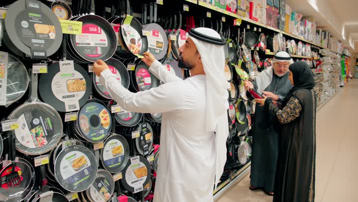 التعاون والترابط الأسري، عائلة عربية خليجية اماراتية ترتدي الزي التقليدي تختار أواني الطبخ داخل متجر أدوات منزلية ، المشاركة في اختيار أدوات المطبخ، مفهوم التسوق العائلي داخل مركز تجاري، الاهتمام بتجهيز المطبخ بأدوات عملية
