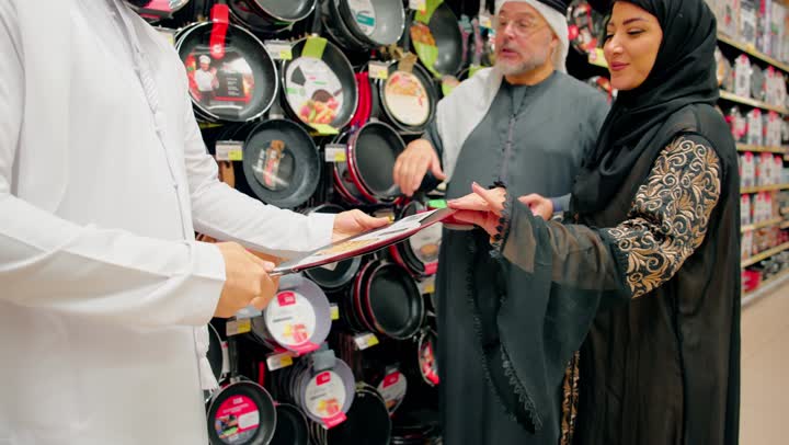 عائلة عربية خليجية اماراتية ترتدي الزي التقليدي تتفقد أواني الطبخ داخل متجر أدوات منزلية ، المشاركة في اختيار المقالي وأدوات المطبخ، التسوق العائلي داخل المركزالتجاري، الاهتمام بتجهيز المطبخ بأدوات عملية، مفهوم التعاون الاسري و الترابط العائلي