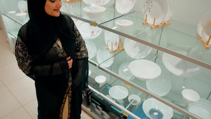 الاهتمام بتجهيز المنزل الأنيق، اختيار الأواني والأدوات المنزلية المناسبة للاستخدام اليومي، تصوير مقرب لسيدة عربية خليجيه اماراتية محجبة تتفقد أدوات منزلية داخل المتجر