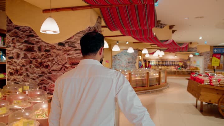 شراء اللوازم والاحتياجات الغذائية، اختيار المكسرات والمواد الغذائية الجافة، رجل عربي خليجي اماراتي يرتدي الزي الكاجوال يتسوق داخل متجر مكسرات