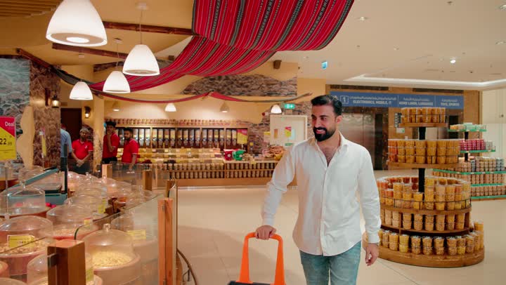 Shopping for various food items, selecting nuts and dry food, an Arab Gulf Emirati man wearing casual attire shopping inside the supermarket.