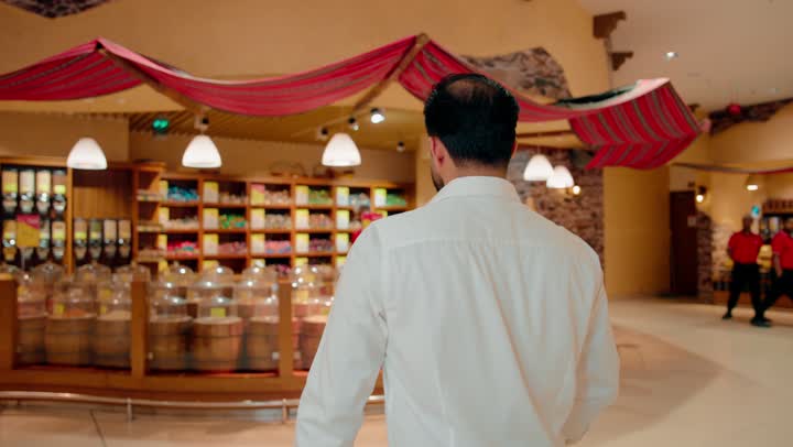 رجل عربي خليجي اماراتي يرتدي الزي الكاجوال يتسوق داخل متجر مكسرات ، بائع يقدم تشكيلة متنوعة من المكسرات الطازجة، اختيار المكسرات والمواد الغذائية الجافة