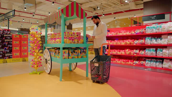 اختيار منتجات الحلويات والسناكس المتنوعة، رجل عربي خليجي اماراتي يرتدي الزي الكاجوال يتجول داخل متجر مواد غذائية حديث، التسوق داخل السوبرماركت