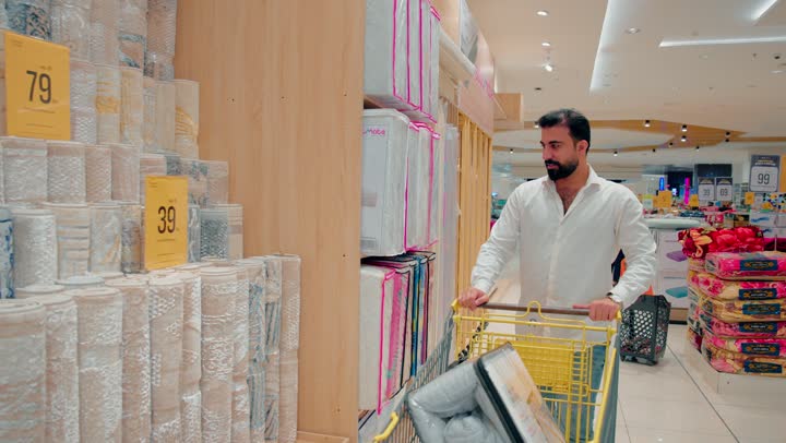اختيار سجاد منزلي مناسب لتجهيز المنزل، رجل عربي خليجي اماراتي يرتدي الزي الكاجوال يتسوق داخل المتجر يقوم بتفقد تشكيلة متنوعة من السجاد المعروض، الاهتمام بجودة المنتجات المنزلية