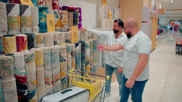Choosing the right carpet to furnish a modern home, two Arab Gulf Emirati men dressed in casual attire are inspecting a variety of carpets inside a home goods store, focusing on the quality of home products, and friends collaborating during the shopping process.