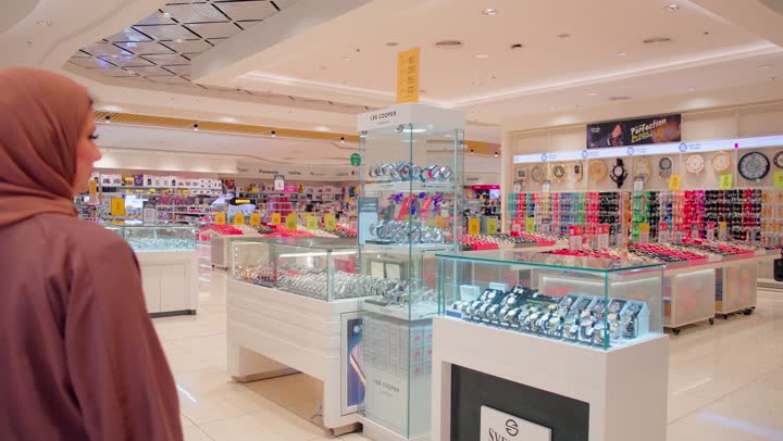 Choosing modern women's accessories, a Gulf Arab Emirati woman in a hijab stands inside a watch store examining a variety of watches displayed in an elegant glass showcase, shopping in modern malls, the concept of elegance and fashion.