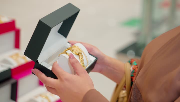 تحليل الخيارات قبل اتخاذ قرار الشراء، مفهوم التسوق الواعي،امرأة عربية خليجية اماراتية تمسك ساعة يد فاخرة ذات تصميم أنيق تقوم بتفقدها لمنتجات الساعات داخل المتجر، الاهتمام بالتفاصيل وجودة المنتج