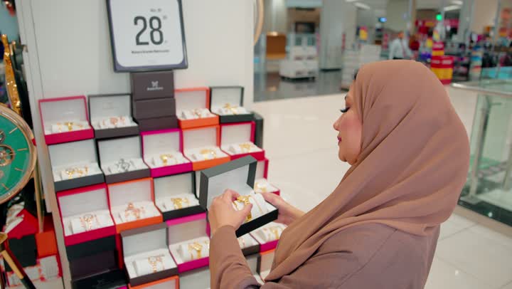 Comparing alternatives before making a purchase decision, the concept of conscious shopping, an Arab Gulf Emirati woman holding a luxurious watch with an elegant design, examining it among the watch products inside the store, attention to detail and product quality.