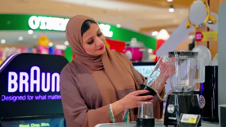 معاينة الجودة و التصميم، اهتمام المستهلك بجودة المنتجات قبل الشراء، امراة عربية خليجيه اماراتية تقف داخل متجر  تقوم بتفقد خلاط كهربائي منزلي، مفهوم التسوق اليومي, اختيار الأجهزة المنزلية المناسبة