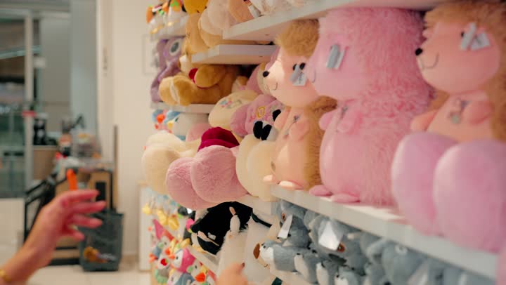 انتقاء ألعاب آمنة ومناسبة، مفهوم التسوق للأطفال، امرأة عربية خليجية اماراتية ترتدي الحجاب و العباءة داخل متجر مخصص لمنتجات الأطفال تقوم بتفقد لعبة دمية وتعاين شكلها وجودتها قبل الشراء