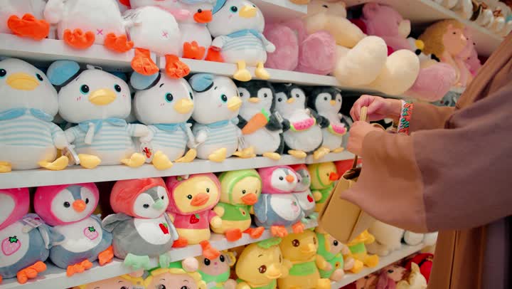 مفهوم التسوق للأطفال، امرأة عربية خليجية اماراتية ترتدي الحجاب و العباءة داخل متجر مخصص لمنتجات الأطفال تقوم بتفقد لعبة دمية وتعاين شكلها وجودتها قبل الشراء، اختيار الألعاب الآمنة والمناسبة