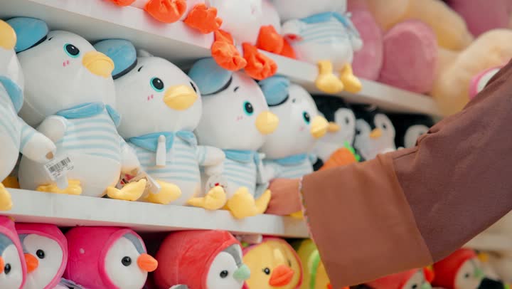 امرأة عربية خليجية اماراتية ترتدي الحجاب و العباءة داخل متجر مخصص لمنتجات الأطفال تقوم بتفقد لعبة دمية وتعاين شكلها وجودتها قبل الشراء، مفهوم التسوق للأطفال، اختيار الألعاب الآمنة والمناسبة