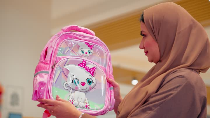 Previewing the design and quality, a veiled Emirati Gulf Arab woman wearing an abaya inside a school supplies store is inspecting a school bag designed for children, preparing for back-to-school, choosing the appropriate supplies for children.