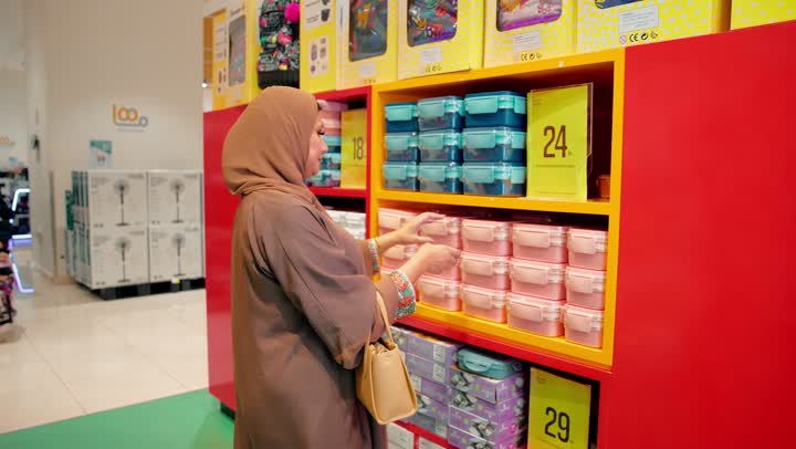 مفهوم التسوق اليومي، التسوق من قسم تنظيم المطبخ، امراة عربية خليجيه اماراتية تقف داخل متجر مستلزمات منزلية تقوم بتفقد علب حفظ الطعام البلاستيكية، اختيار الأدوات المنزلية المناسبة، تنظيم وحفظ الطعام