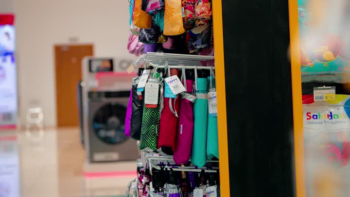 Protection from the sun and rain, choosing the right personal accessories, a close-up shot of a Gulf Arab woman in a hijab inside a store selecting a colorful umbrella with decorative designs, the concept of daily shopping.