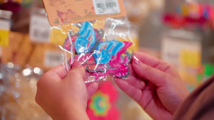 المنتجات المخصصة للأطفال، مفهوم التسوق لمستلزمات الأطفال، تصوير مقرب ليد امرأة عربية خليجية اماراتية تمسك عبوة تحتوي على إكسسوارات شعر ملونة للأطفال داخل المتجر، العناية بالمظهر الشخصي، الإكسسوارات النسائية