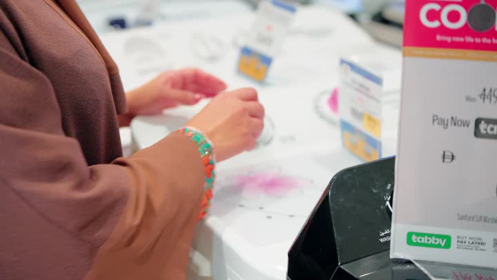 تصوير مقرب لامرأة عربية خليجية امارتية داخل متجر أجهزة منزلية تقوم بتفقد غسالة ملابس ومراجعة مواصفاتها قبل الشراء، مفهوم التسوق الذكي، اختيار الأجهزة المنزلية المناسبة