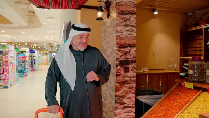 شراء المواد الغذائية، ثقافة الغذاء العربي، مفهوم التسوق الواعي، المنتجات الغذائية الطازجة، رجل عربي خليجي اماراتي يرتدي الزي التقليدي داخل متجر مواد غذائية يقوم باختيار التمور والتأكد من جودتها، نمط حياة صحي