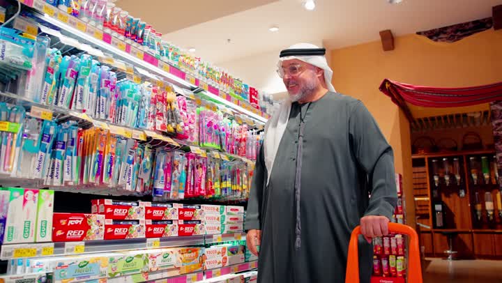 اختيار المنتجات الصحية، العناية بنظافة الفم والأسنان، رجل عربي خليجي اماراتي يقف داخل سوبرماركت يقوم باختيار فرشاة أسنان من رف منتجات العناية الشخصية، مفهوم التسوق اليومي، منتجات العناية الشخصية