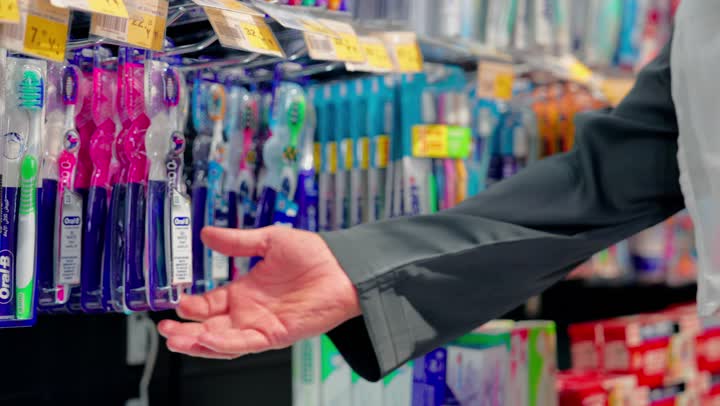 Oral and dental hygiene, a close-up shot of the hand of an Emirati Arab man standing inside a supermarket choosing a toothbrush from the personal care products shelf, the concept of daily shopping, selecting healthy products, personal care products.