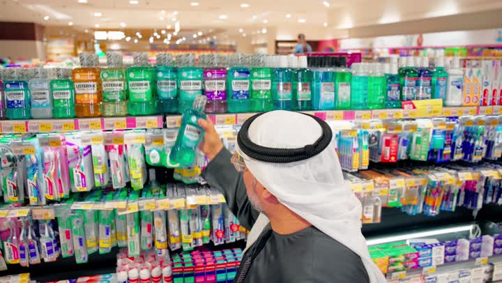 اختيار منتجات العناية الشخصية والنظافة المناسبة، مفهوم التسوق اليومي، تصوير مقرب لرجل عربي خليجي اماراتي يقف داخل سوبرماركت يقوم بقراءة عبوه منتج عناية شخصية من على الرفوف، متاجر البيع بالتجزئة