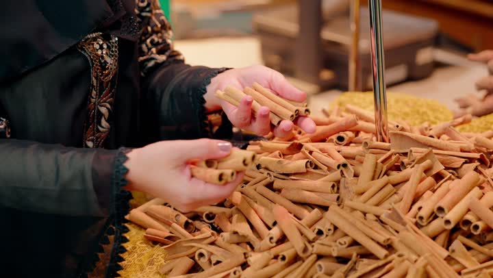 ثقافة الغذاء والطبخ، تصوير مقرب لامرأة عربية خليجيه اماراتية محجبة تقف داخل متجر توابل تقوم بشم رائحة الأعشاب، اختيار المنتجات عالية الجودة، المنتجات الطبيعية والعضوية، نمط حياة صحي، أسواق ومحلات المواد الغذائية