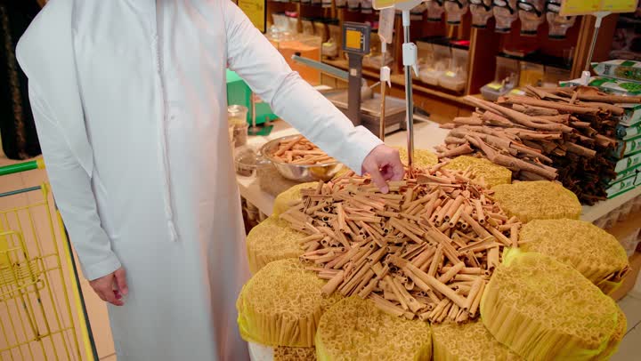 أسواق ومحلات المواد الغذائية، رجل عربي خليجي اماراتي يرتدي الزي التقليدي يقف داخل متجر توابل يقوم بشم رائحة الأعشاب للتأكد من جودتها،مفهوم التسوق الواعي، المنتجات الطبيعية والعضوية، نمط حياة صحي