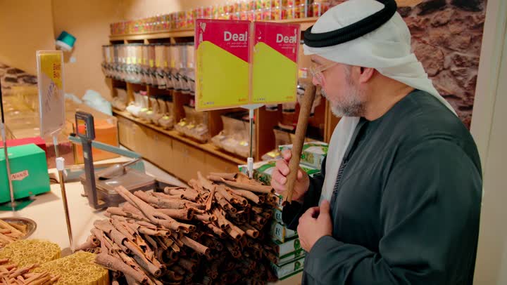ثقافة الغذاء العربي، رجل عربي خليجي اماراتي يرتدي الزي التقليدي يقف داخل متجر توابل يقوم باختيار عيدان القرفة الطبيعية، المنتجات الطبيعية والعضوية، الأعشاب والتوابل ومكونات الطهي، نمط حياة صحي، أسواق ومحلات المواد الغذائية