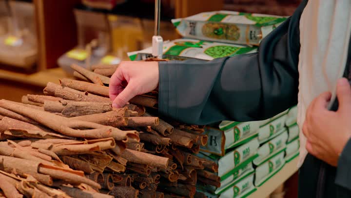 مفهوم التسوق والمنتجات العضوية، تصوير مقرب لرجل عربي خليجي اماراتي يختار عيدان القرفة الطبيعية داخل سوبرماركت، تفاصيل التوابل التقليدية وجودتها، مكونات الطهي الصحي، أعشاب وتوابل طبيعية، نمط حياة صحي، ثقافة الغذاء والطبخ