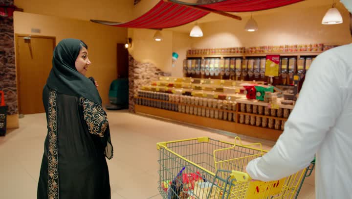 الاستفاده من التخفيضات والعروض على المنتجات، عرض المنتجات والمواد الغذائيه على الارفف في السوبرماركت، أسرة عربيه خليجيه اماراتية مستمتعه بتبضع اللوازم المنزليه، ايماءات الفرح والسعاده لقضاء أوقات ممتعه برفقه العائله
