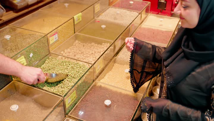 الاستفاده من التخفيضات والعروضات على المنتجات في الامارات العربية، الوجبات الخفيفه والسناكات الصحيه اللذيذه، تصوير مقرب لامراه عربيه خليجيه اماراتية محجبة ترتدي العباءة تقوم بشراء المكسرات من السوبرماركت