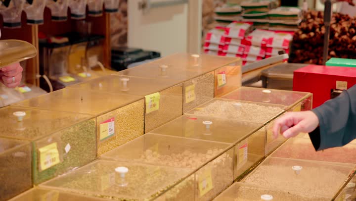 التدقيق في جودة الحبوب قبل الشراء، شراء المواد الغذائية، تصوير مقرب ليد بائع عربي خليجي اماراتي يقوم بتعبئة المكسرات لعميل داخل المتجر