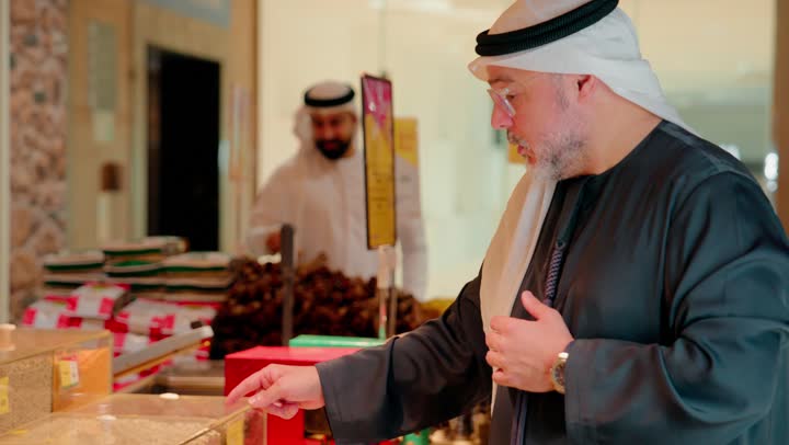 اختبارجودة الحبوب قبل الشراء، شراء المواد الغذائية، تصوير مقرب ليد بائع عربي خليجي اماراتي يقوم بتعبئة المكسرات لعميل داخل المتجر