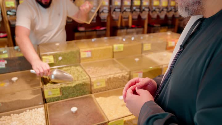 شراء المواد الغذائية، تصوير مقرب ليد بائع عربي خليجي اماراتي يقوم بتعبئة المكسرات لعميل داخل المتجر، اختبار جودة الحبوب قبل الشراء