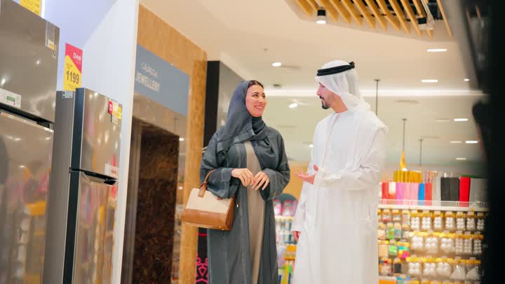 زوجان عربيان خليجيان اماراتيان يرتديان الزي التقليدي يتبادلان الحديث أثناء التسوق، مناقشة واختيار الأجهزة المنزلية قبل الشراء، أجواء تسوق عائلية، تعاون واتخاذ قرار مشترك، ايماءات السعادة والسرور